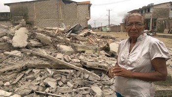 Woman stands beside the rubble that was once her home in Ecuador.