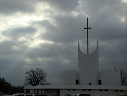 Photo of a church's pinnacle beneath a cloudy, sunlit sky.