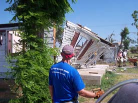 A volunteer in a blue shirt at a site affected by severe storm damage.