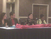 Several people at an oblong table with a red covering and microphone, as part of a panel.