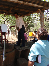 Douglas stands on a stool to pump a new well in front of several people.