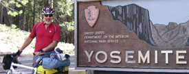 A man standing with a bike beside a "Yosemite National Park" sign.