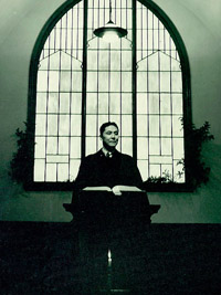 A black and white photo of Walter Soboleff, standing from a pulpit under a stained glass window.