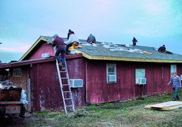 A group of people on a roof of a red-colored house, working.