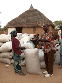 A group of people near near a village house surrounded by large bags of grain.