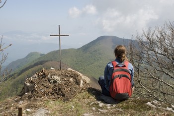 a young woman sits on a mountain looking a cross