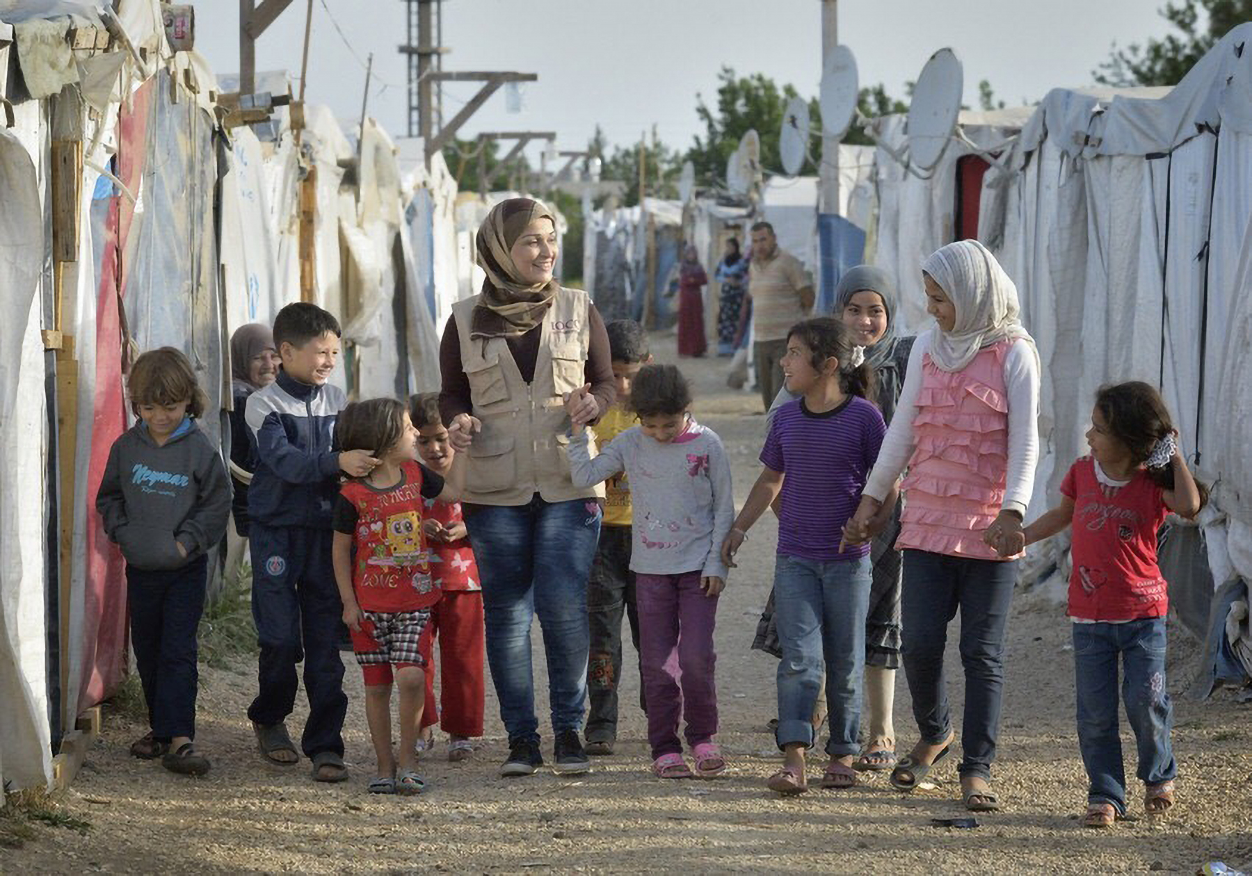 Ahlam Al Khaled, a health and nutrition educator for International Orthodox Christian Charities, walks with children in a settlement of Syrian refugees in Minyara, a village in the Akkar district of northern Lebanon. Lebanon hosts some 1.5 million refugees from Syria, yet allows no large camps to be — Paul Jeffrey/ACT