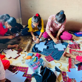 This image shows Nepali women sitting on the floor in a circle sewing sanitary pads