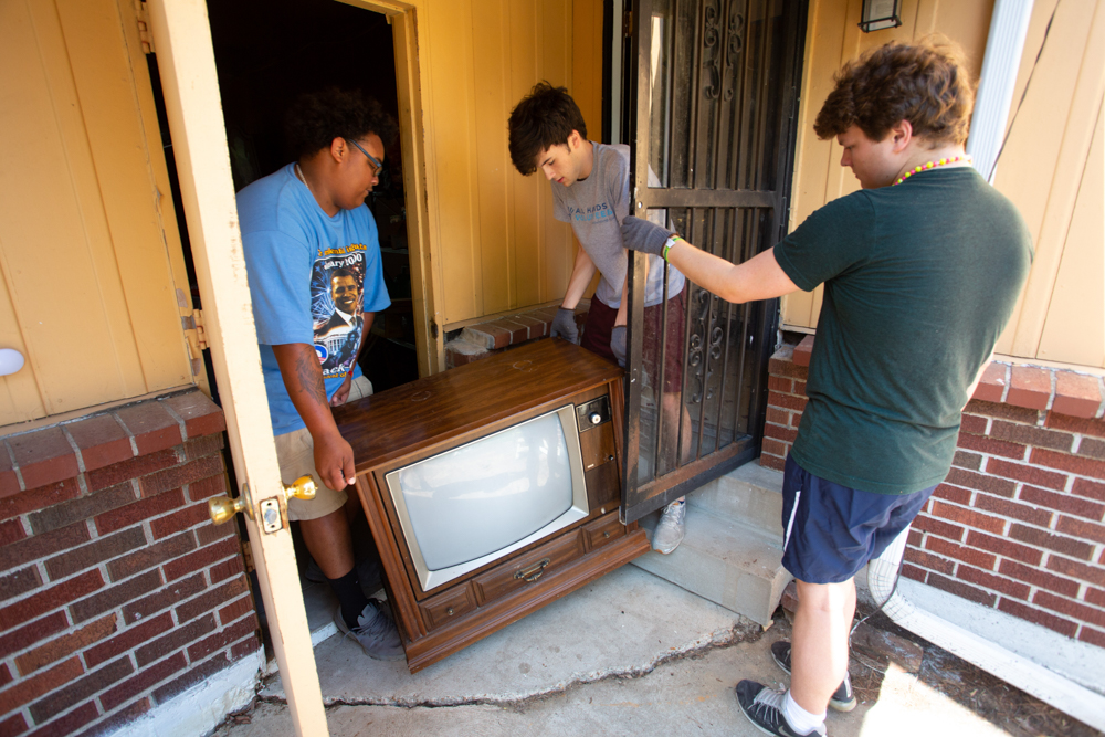 Caleb Morris, Evan Holmes, and Grady Stevens, of Louisville, KY, carry a TV to a dumpster near Ferguson, MO on Tuesday, June 19, 2018. (Photo by Michael Whitman)