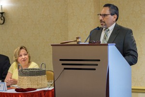 Tony De La Rosa, interim executive director of the Presbyterian Mission Agency, addresses the PMA Board following the announcement of his appointment alongside PMAB Chair Marilyn Gamm (seated.)