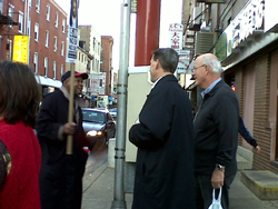 Two men talk to another man holding a protest sign on the street.