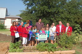 A group of people standing in a garden beside a newly-laid plot and a sign.