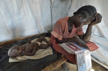 Nyanthem Mayol stares at photos of her relatives while her baby sleeps at her side in a temporary shelter near Ajoung Thok, South Sudan, where they fled after fighting broke out in their home town of Bentieu in late 2013. 