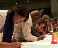A group of people bending over a table, writing.