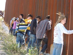Young Adult Volunteers pray at the fence separating the United States and Mexico. 