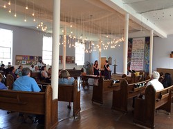 Co-pastors Rebecca Blake (left) and Karen Rohrer (right) in Beacon’s sanctuary that features ‘rolling pews’ and 150 hanging light bulbs—a nod to both the neighborhood’s industrial legacy and the church’s history: they cast light out both sides of sanctuary and into the street. 