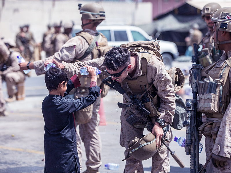 A Marine with Special Purpose Marine Air-Ground Task Force-Crisis Response-Central Command (SPMAGTF-CR-CC) and a child spray water at each other during an evacuation at Hamid Karzai International Airport, Kabul, Afghanistan, Aug. 21. U.S. service members are assisting the Department of State with an orderly drawdown of designated personnel in Afghanistan. (U.S. Marine Corps photo by Sgt. Samuel Ruiz).