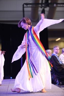 a liturgical dancer spins around in a flowing white dress and colorful scarf