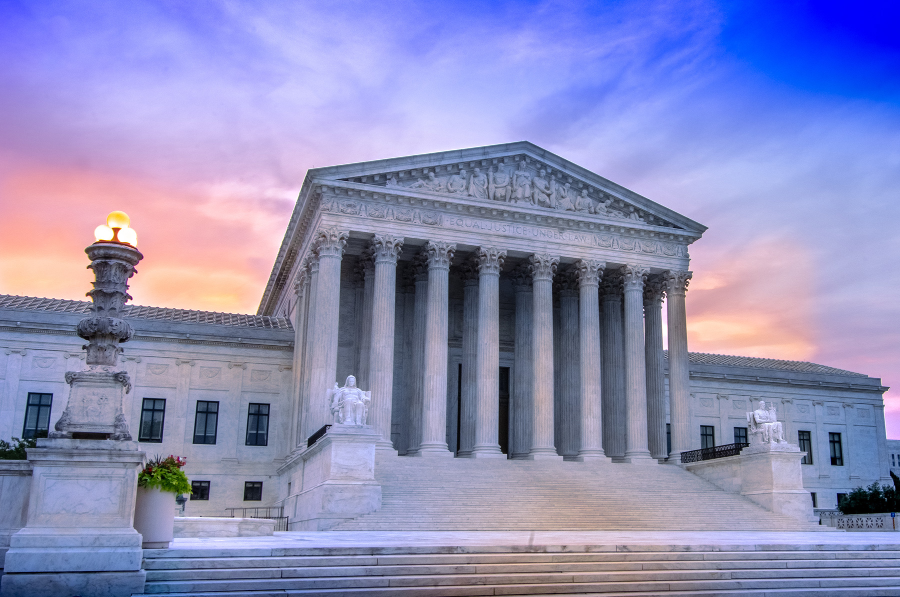View of marble columns and greek classical architecture of the United States Supreme Court building with sunrise in background.